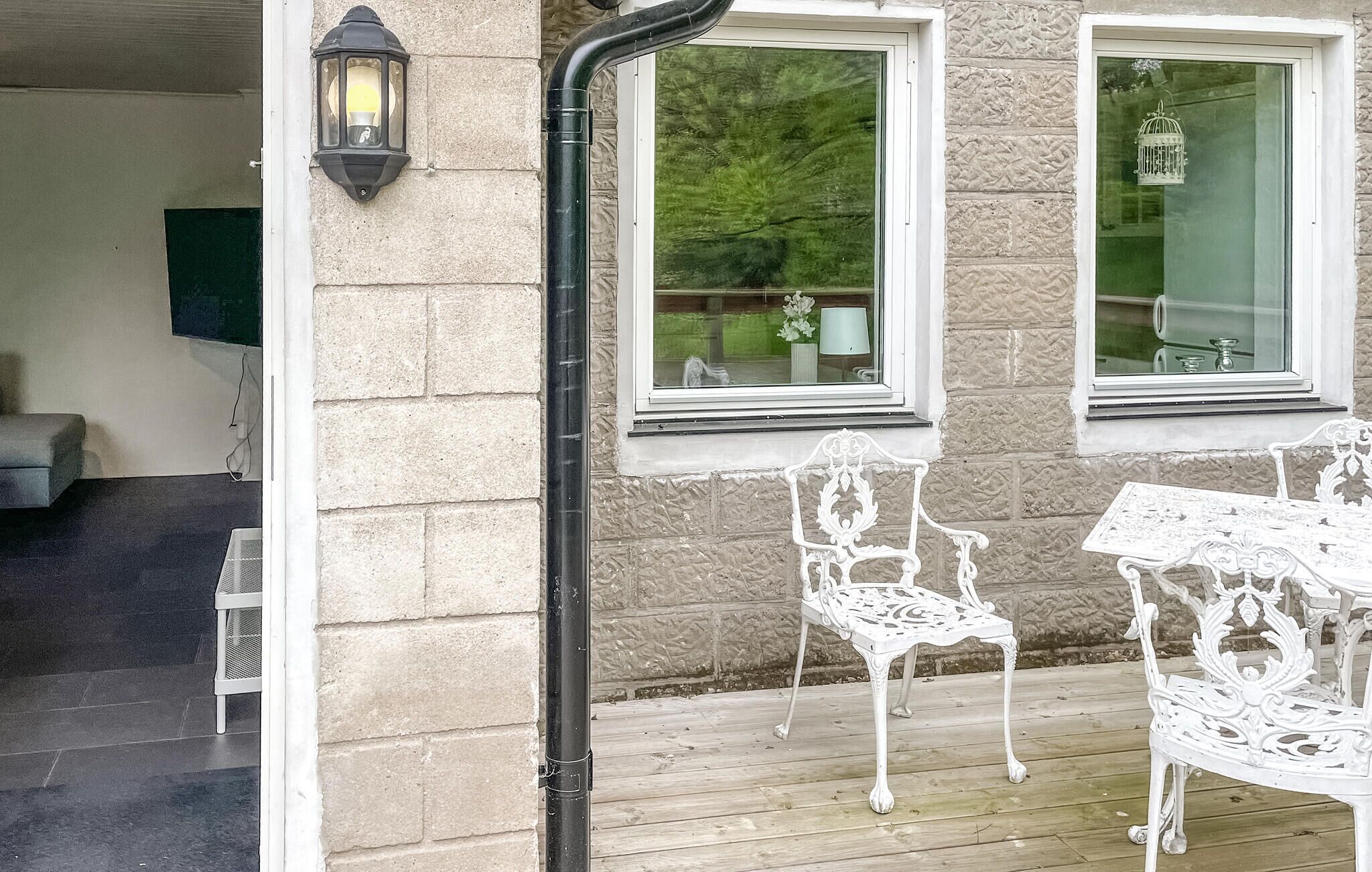 Un espacio al aire libre techado con una terraza de madera, sillas de metal blanco y una mesa.