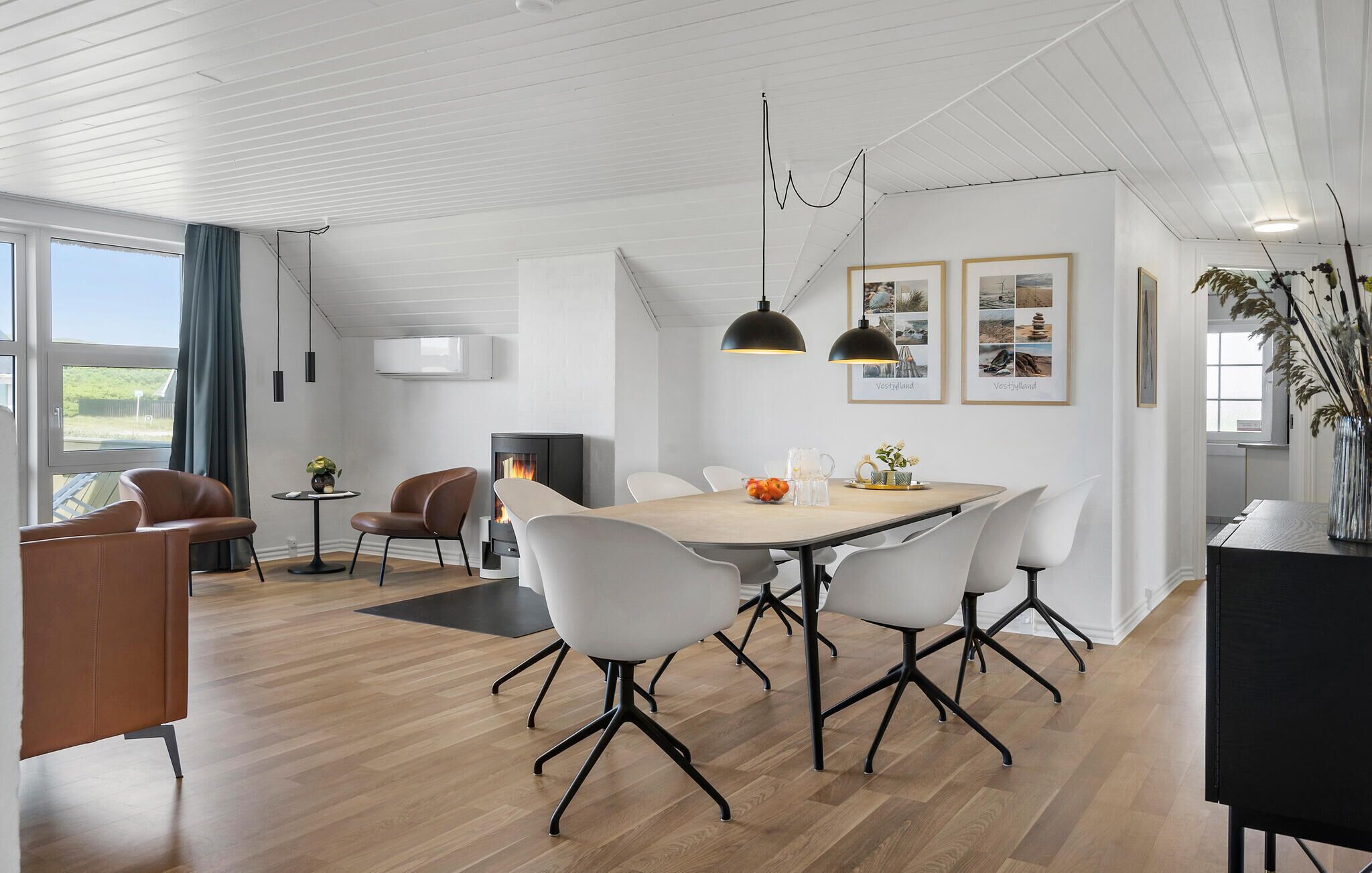 A modern dining area with a wooden table, white chairs, and pendant lighting.