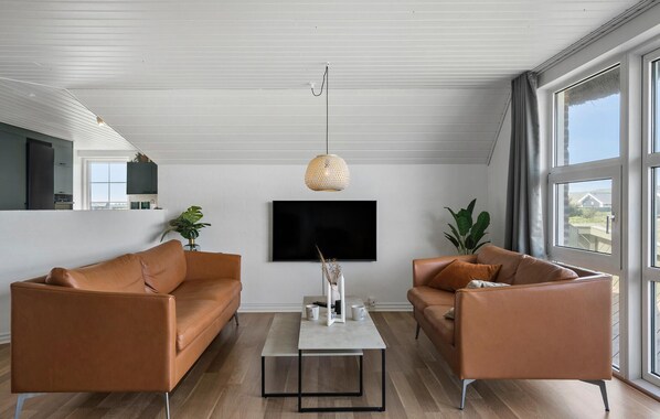A modern living room with two leather sofas, a coffee table, a TV, and a large window with a view.