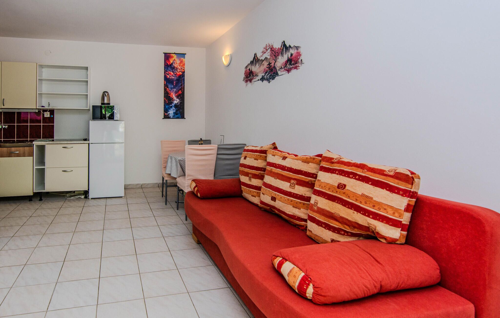 Un espace de vie compact comprenant un coin cuisine, un canapé agrémenté de coussins à motifs et une œuvre d’art accrochée au mur.