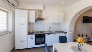 A modern kitchen with white cabinetry, a built-in oven, a stove, and a sink. There is a dining area with a table and chairs, and a TV mounted on the wall. - Lovely apartment in Ploce with WiFi (Ploce)