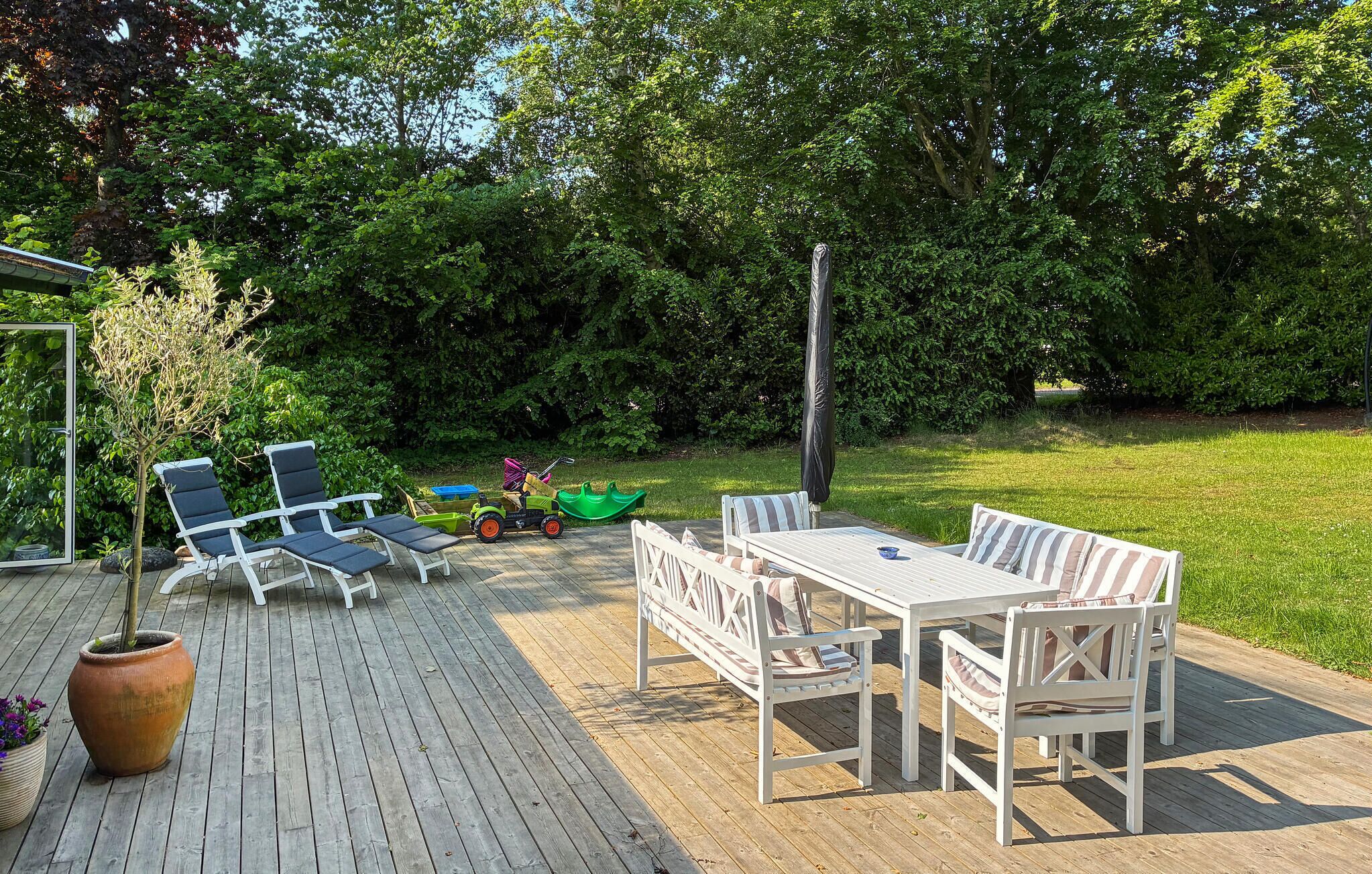 A wooden deck with a table and chairs, surrounded by lush greenery and trees.