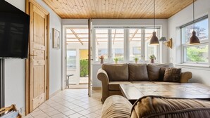 Una sala de estar moderna con techo de madera, un sofá, una mesa y ventanas grandes.