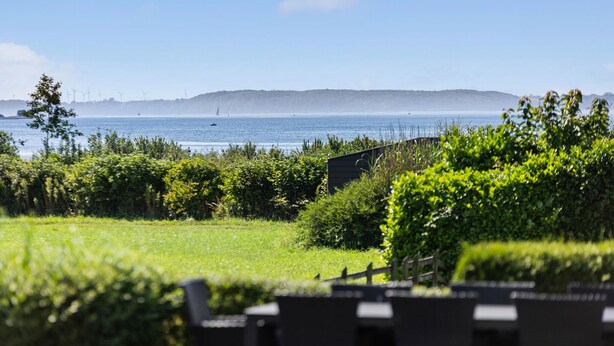Vista costera con zona verde, un edificio pequeño y una masa de agua con barcos.