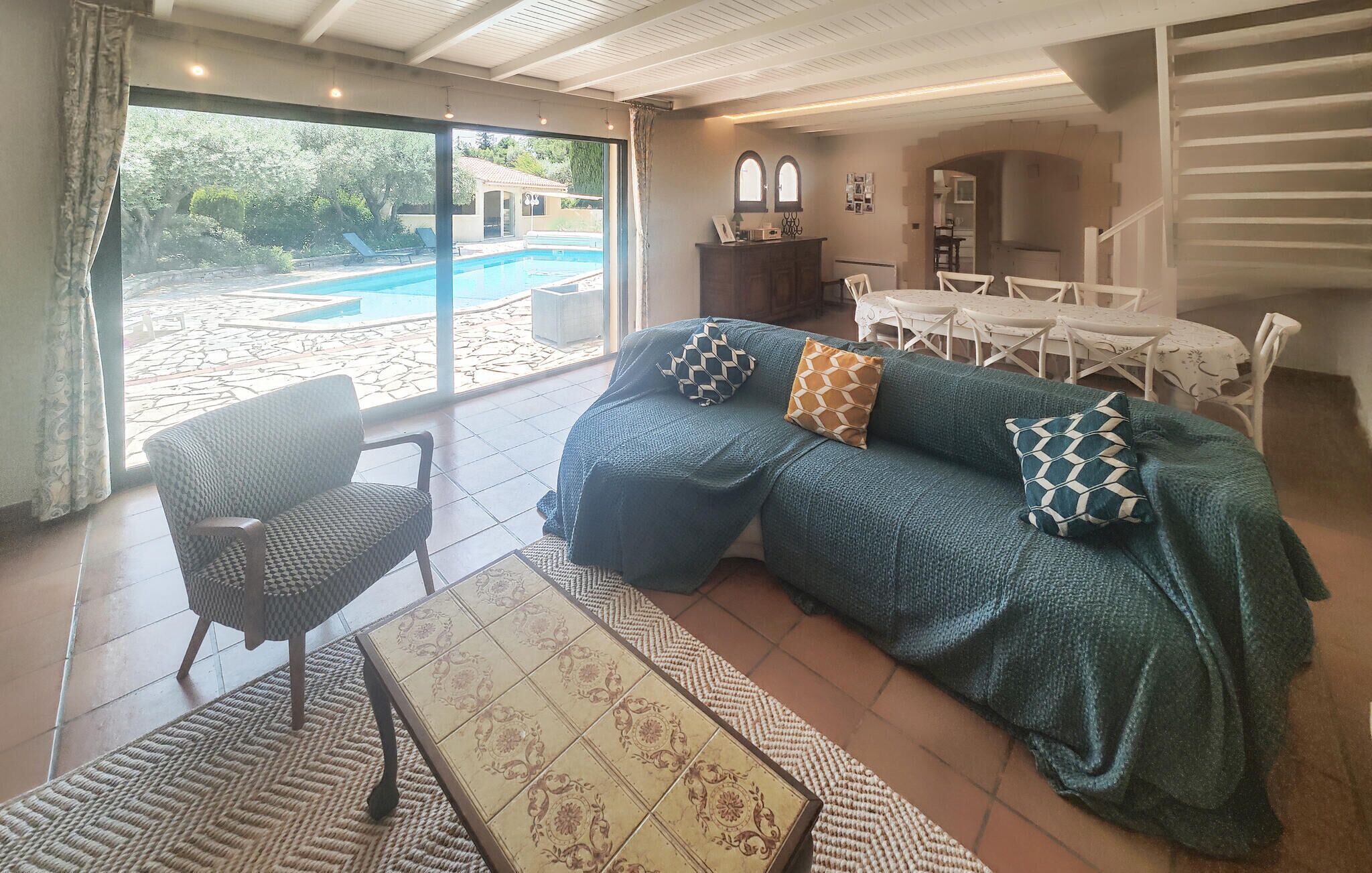 Un salón con un ventanal grande, un sofá, una silla, una mesa y vistas a una piscina.