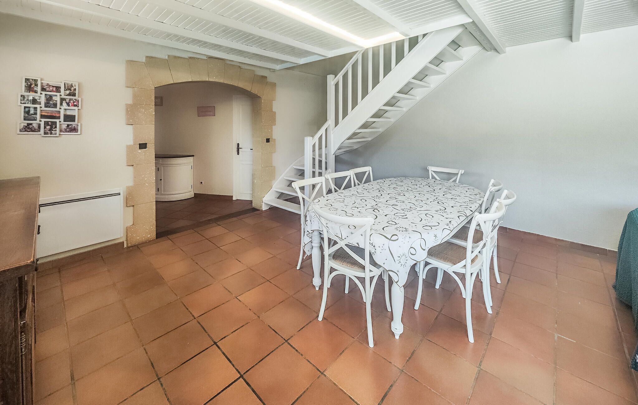 Een eetgedeelte met een witte tafel en stoelen, een trap en een betegelde vloer.