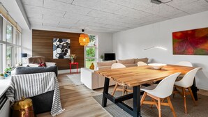 Una sala de estar moderna con una mesa de comedor de madera, sillas blancas, un sofá y un televisor.