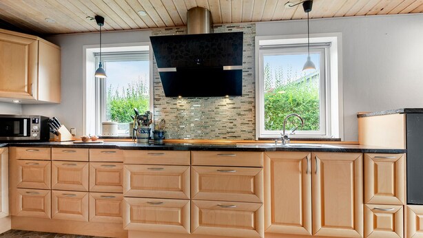 Una cocina moderna con una isla grande, armarios de madera, salpicadero de piedra y dos ventanas que ofrecen luz natural.