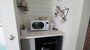 A compact kitchen with a microwave, coffee maker, and a black refrigerator. - Blackwater Bay beach tiny homes (Bolivar Peninsula)