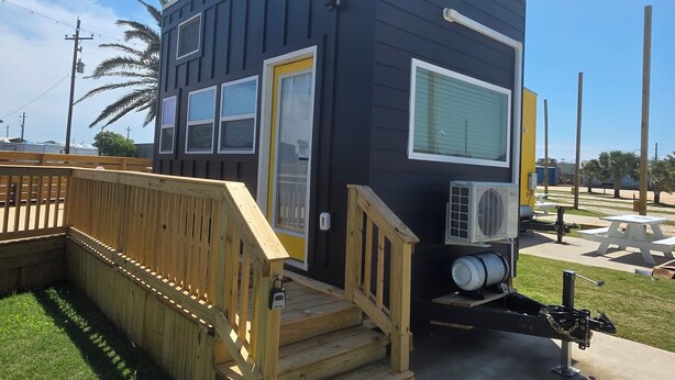 A small, dark-colored building with a wooden deck and a single door. - Blackwater Bay beach tiny homes (Bolivar Peninsula)