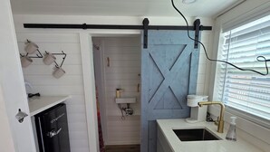 A compact kitchen with a black refrigerator, a blue barn-style door, and a sink with a soap dispenser. - Blackwater Bay beach tiny homes (Bolivar Peninsula)