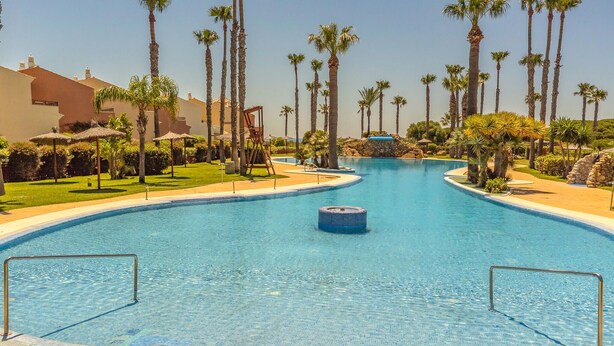 A large, clear swimming pool with a central hot tub, surrounded by palm trees and a well-maintained lawn. - Awesome home in Tarifa with outdoor swimming pool (Tarifa)