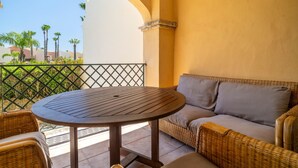 A balcony with a round wooden table and wicker furniture, overlooking a landscaped area with palm trees. - Awesome home in Tarifa with outdoor swimming pool (Tarifa)