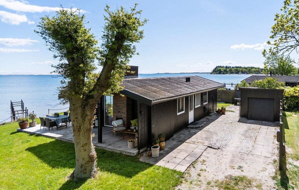 A wooden cabin with a deck overlooking a lake, a small outdoor seating area, and a fenced garden.