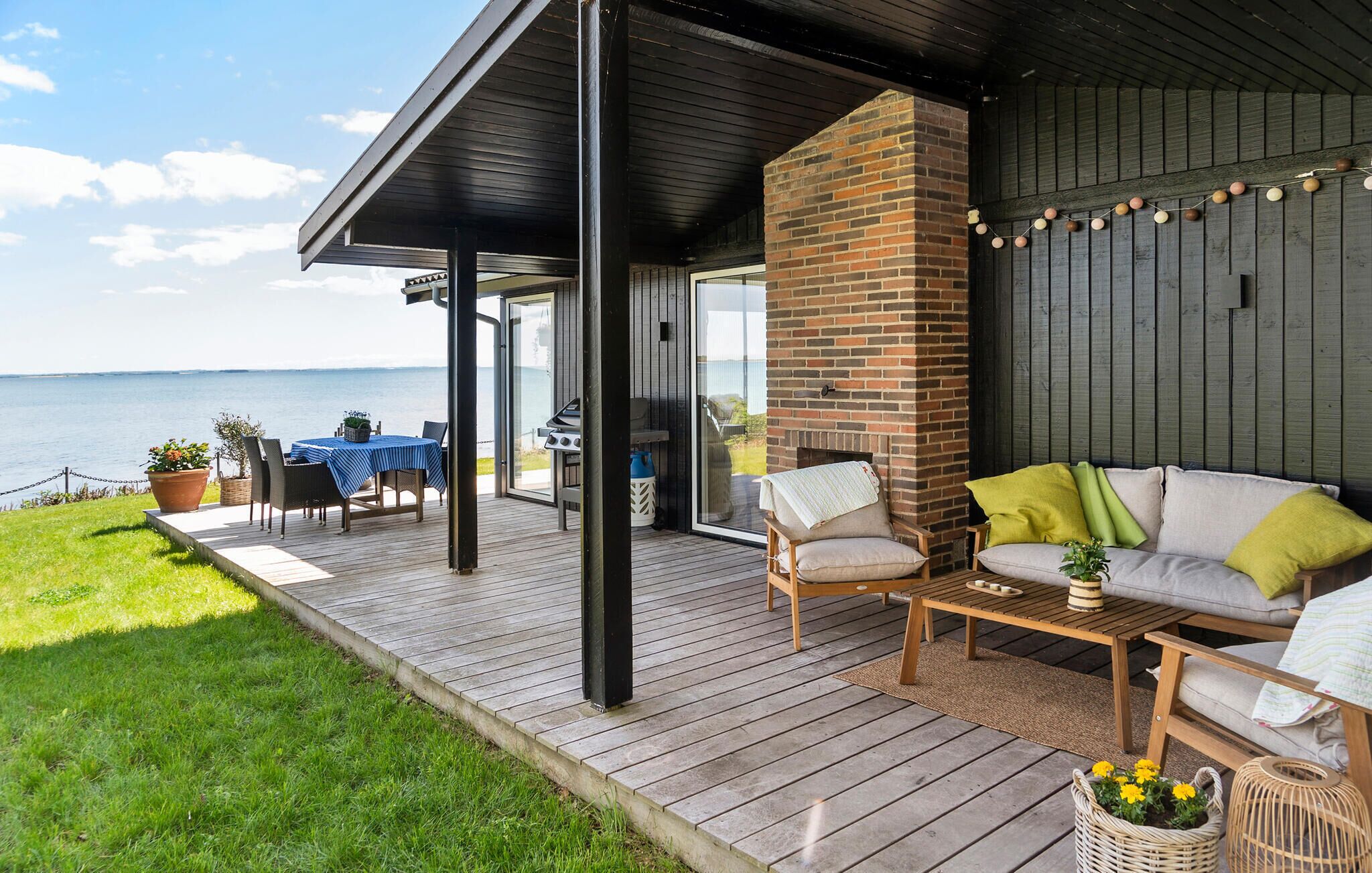 Ein überdachter Außenbereich mit einer Holzterrasse, einem Kamin aus Backsteinen und Blick auf das Meer.