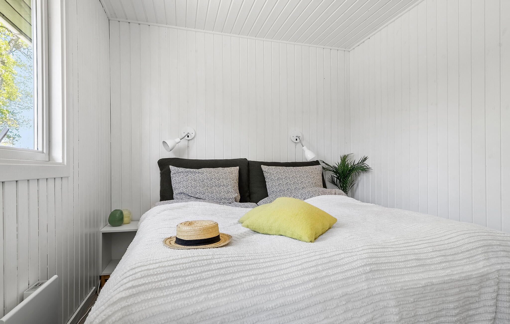 A bedroom with a bed, a window, a radiator, and a plant.