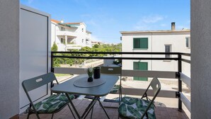 A balcony with a table and two chairs, overlooking a residential area with white buildings and green shutters. - One bedroom cozy apartment in Betina (Betina)