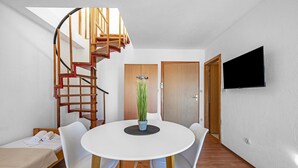 A modern room with a spiral staircase, a round dining table with chairs, a bed with a white mattress, and a flat-screen TV mounted on the wall. - One bedroom cozy apartment in Betina (Betina)