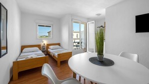 Ein kleiner, moderner Raum mit zwei Holzbett, einem runden Esstisch mit Topfpflanze und Blick auf den Balkon.