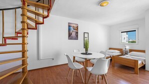 Ein modernes Zimmer mit einer Wendeltreppe aus Holz, einem runden Esstisch mit Stühlen, einem Bett mit Holz-Kopfteil und einem Fenster mit Meerblick.