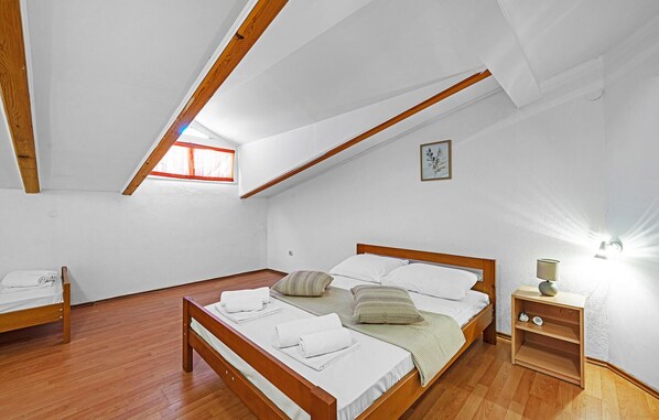 A bedroom with a wooden bed, a small bedside table, a nightstand, a window with curtains, and a ceiling light.
