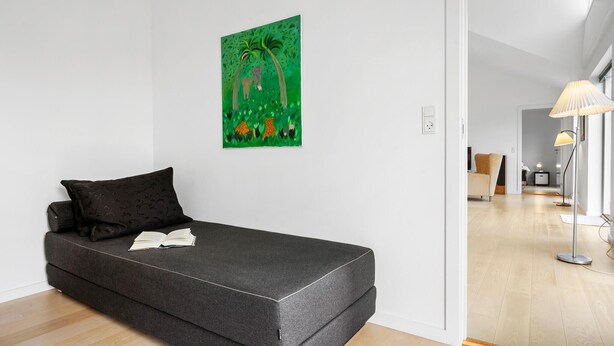 A minimalist room with a dark grey sofa, a green abstract painting, and a modern lamp.