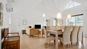 Ett rymligt vardagsrum med ett matbord i trä, beige stoppade stolar och hängande lampor.