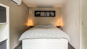 A narrow room with a bed, two bedside lamps, a shelf with books and a vase, and a wall-mounted air conditioner. - 2 bedroom nice home in Ochten (Ochten)