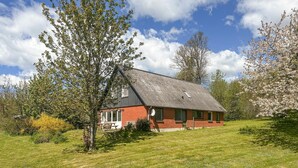 Une maison de plain-pied avec un toit en pente, entourée d’une pelouse et d’arbres.