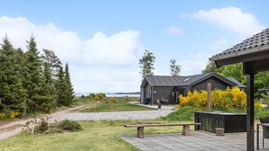 A building with a dark exterior, a gravel path leading to it, and a bench in the foreground. - 3 bedroom cozy home in Højslev (Højslev)
