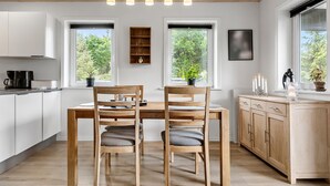 A modern kitchen with a wooden dining table, two chairs, a coffee machine, and a potted plant. - 3 bedroom cozy home in Højslev (Højslev)