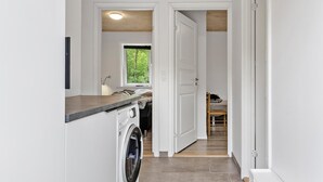 A laundry area with a washing machine, a window with a view of greenery, and a wooden ceiling. - 3 bedroom cozy home in Højslev (Højslev)