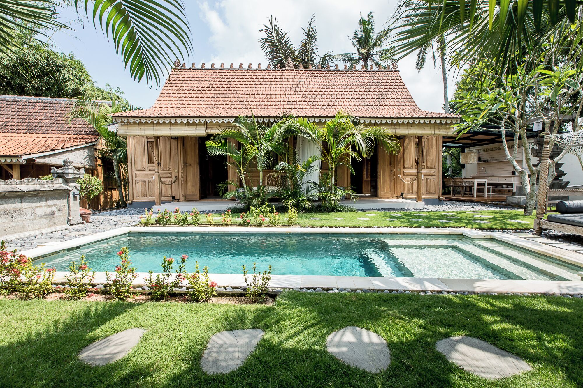 A traditional wooden house with a tiled roof, a swimming pool, and lush greenery.