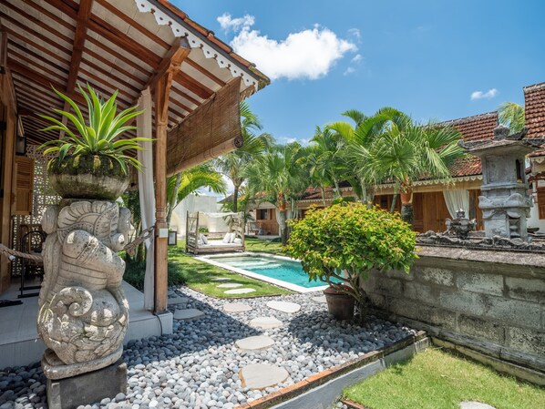 A traditional courtyard with a stone statue, a small pool, and palm trees. - Nido Boutique Cottage (Canggu)