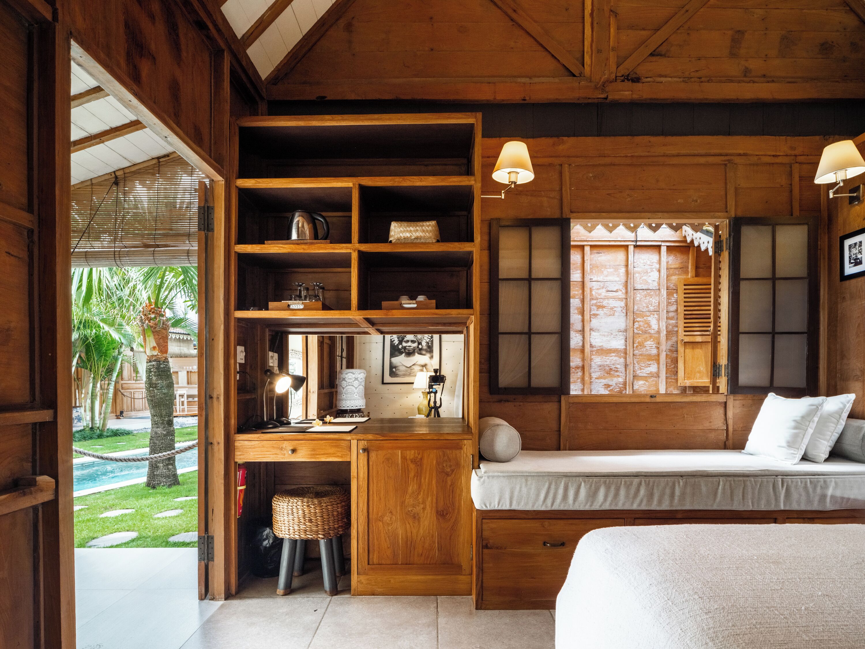 A wooden room with a bed, desk, shelves, and a window with shutters.