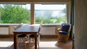 A dining area with a table and chairs, large windows with a view of trees and a body of water, and a wicker chair with a cushion. - Amazing home in åkersberga with WiFi (Åkersberga)