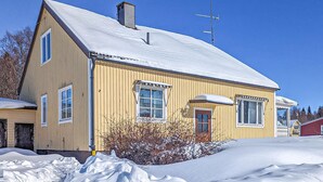 A yellow wooden house with a snow-covered roof and a chimney, surrounded by snow. - Cozy home in Bastuträsk with WiFi (Bastuträsk)