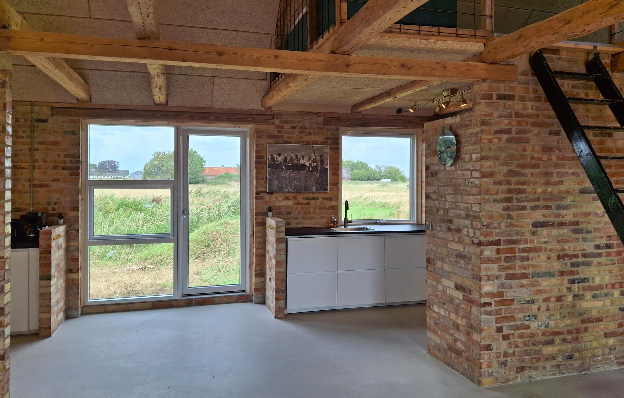 Une cuisine dotée de grandes fenêtres, d’un mur en briques et d’un plafond en bois.