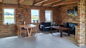 A rustic interior with exposed brick walls, a wooden ceiling, a round wooden table with chairs, a black leather sofa, and a small wooden coffee table. - Nice home in Erslev with WiFi (Erslev)