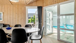 A modern room with a wooden ceiling, a round table with chairs, a large sliding glass door to a pool, and a view of a house and trees outside. - Pet-friendly home in Hejls with sauna (Hejls)