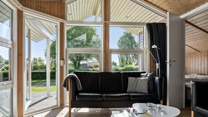 A modern room with a black leather sofa, a small white table, and a large window offering a view of a garden and trees. - Pet-friendly home in Hejls with sauna (Hejls)