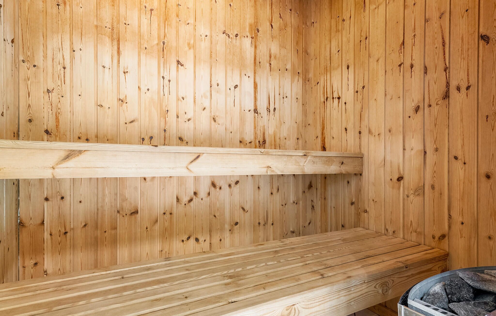 A wooden sauna with a bench and a stone firebox.