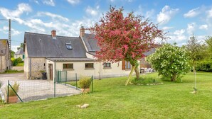 A house with a stone facade, a tiled roof, and a fenced garden with flowering trees. - Charmante maison de Campagne (Méautis)
