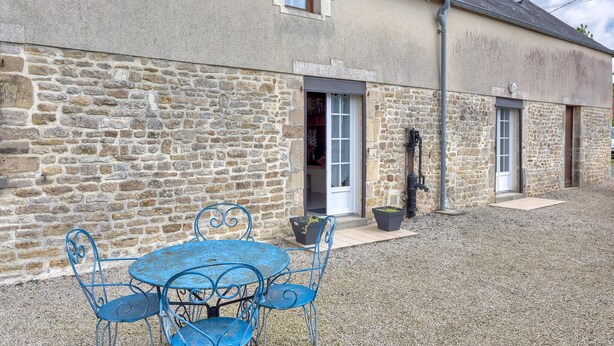 A stone building with a gravel courtyard, a blue metal table and chairs, and a water pump. - Charmante maison de Campagne (Méautis)