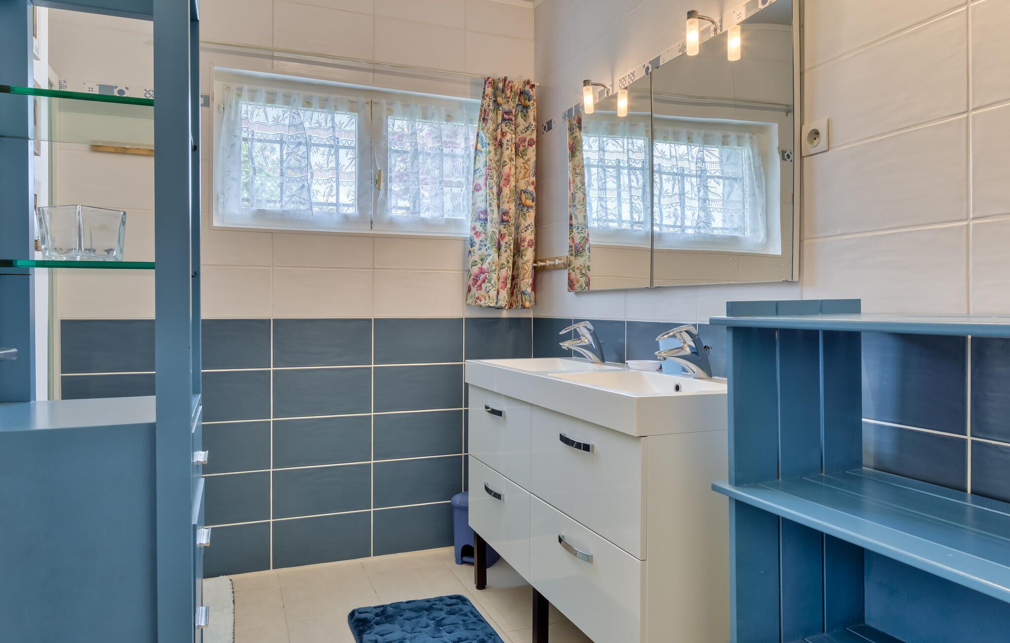 Une salle de bain moderne avec un grand miroir, deux vasques et un meuble-lavabo bleu.