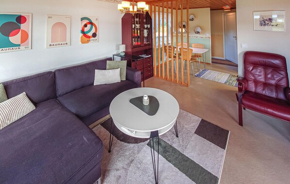 A living room with a sofa, a round coffee table, a red leather chair, a cabinet, and a dining area with a table and chairs. - Awesome home in Kramfors with house sea view (Kramfors)