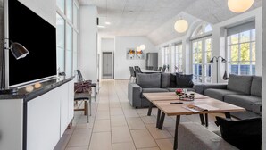 A modern living room with a large flat-screen TV, grey sofas, a wooden coffee table, and a dining area with a large table and chairs. - Pet friendly home in Ulfborg with sauna (Ulfborg)