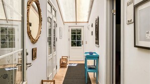 Un pasillo con suelo de madera, una mesa azul con un cuenco y un espejo grande a la izquierda.