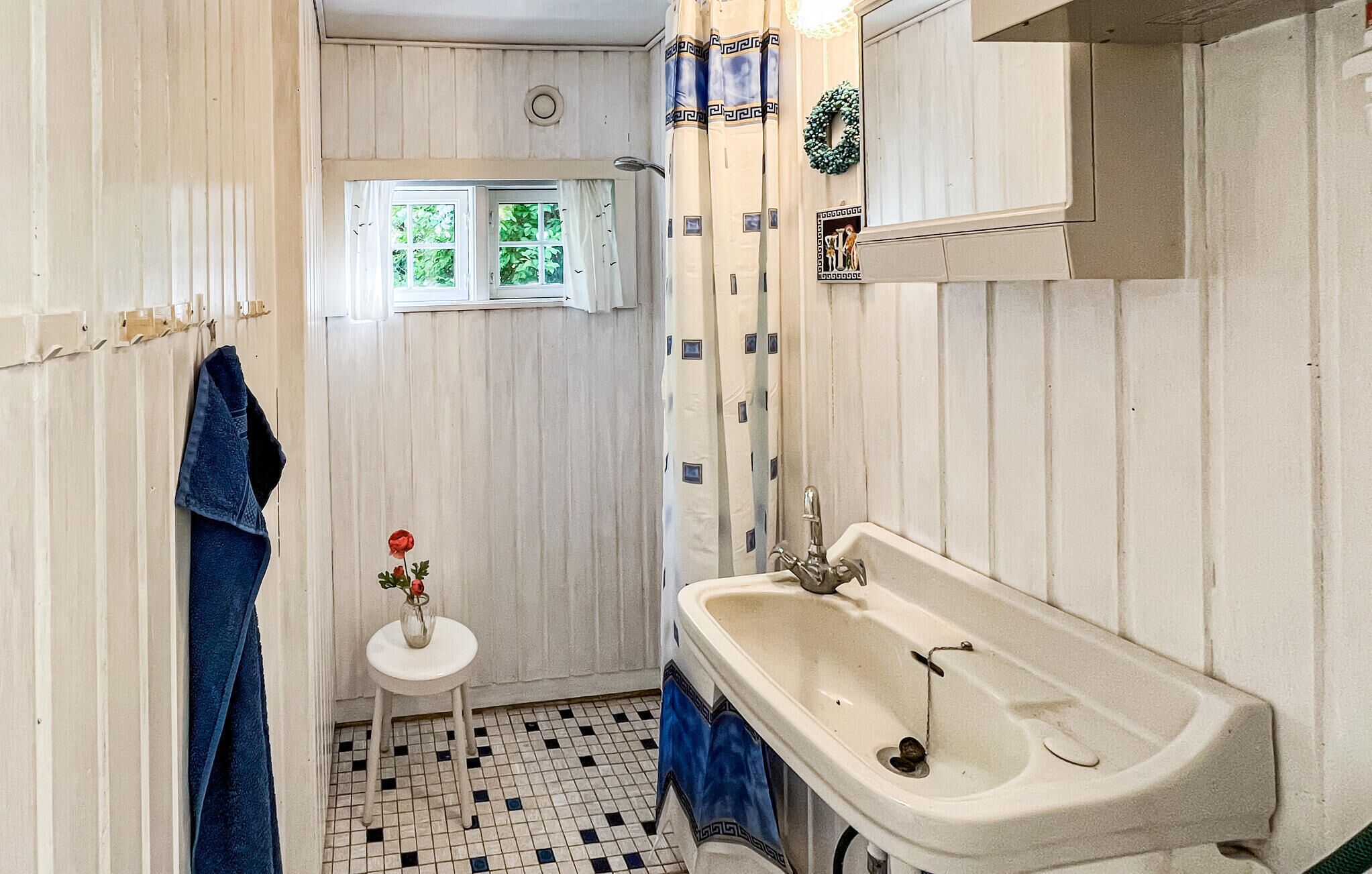 Een badkamer met een wit wastafel, een klein rond tafeltje met een bloemenvaas, en een raam met gordijnen.