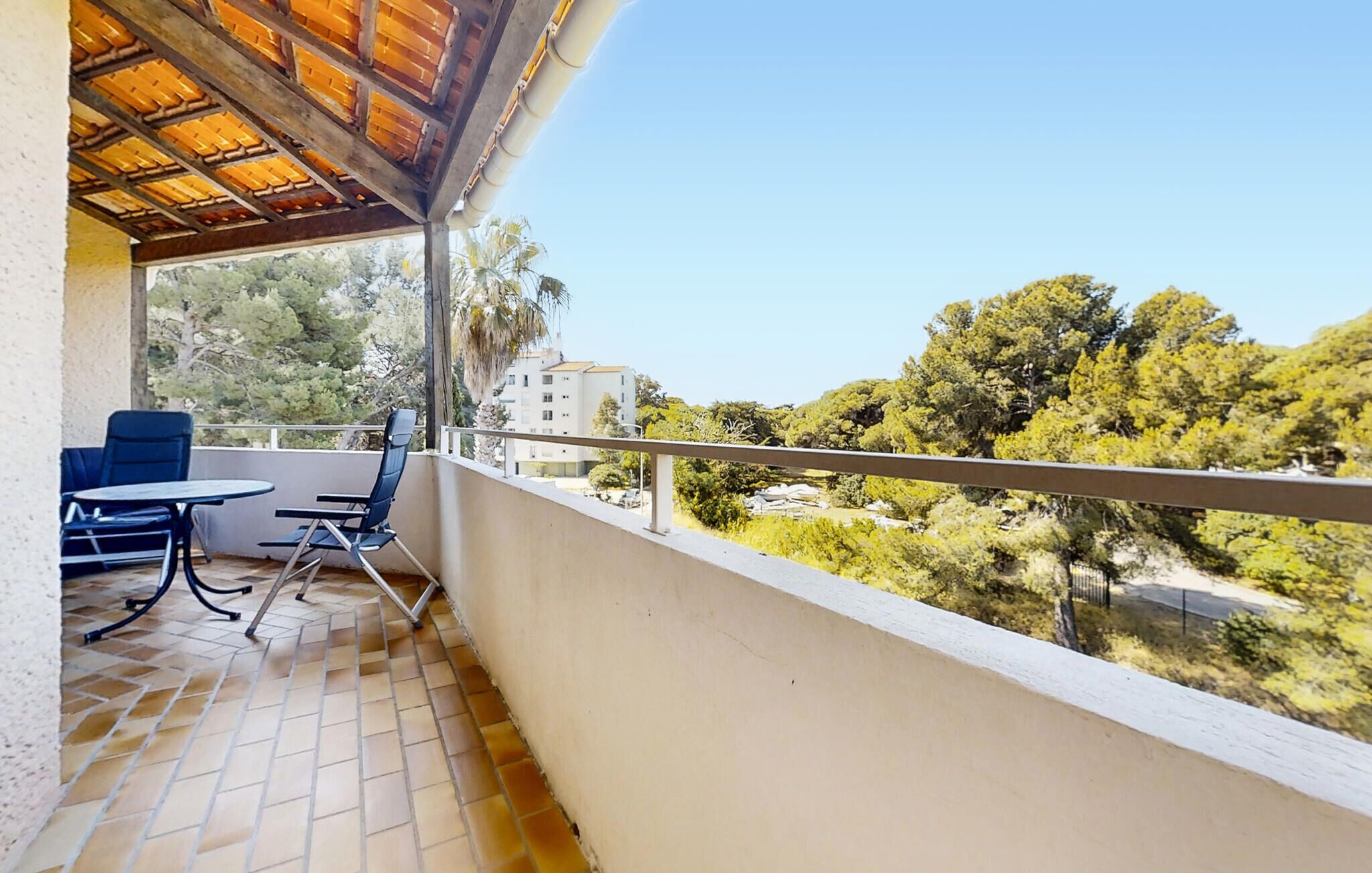 A balcony with a tiled floor, two chairs, a small table, and a wooden pergola.